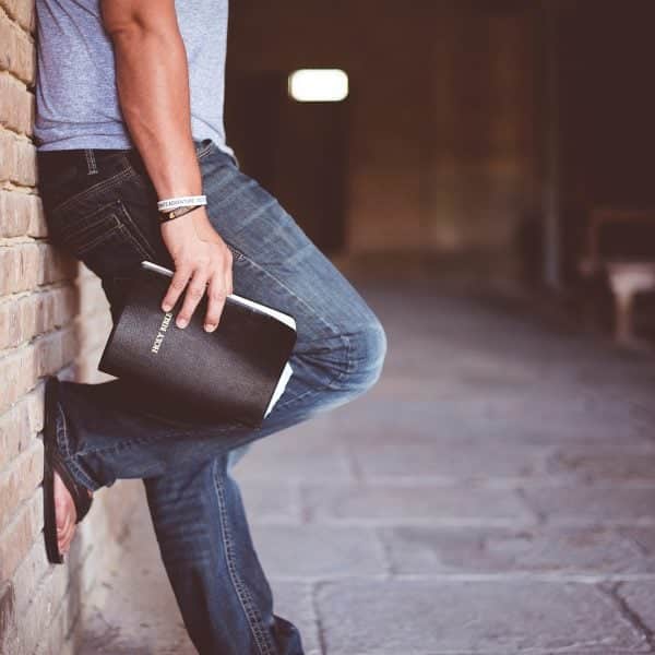 Man leaning against wall holding bible